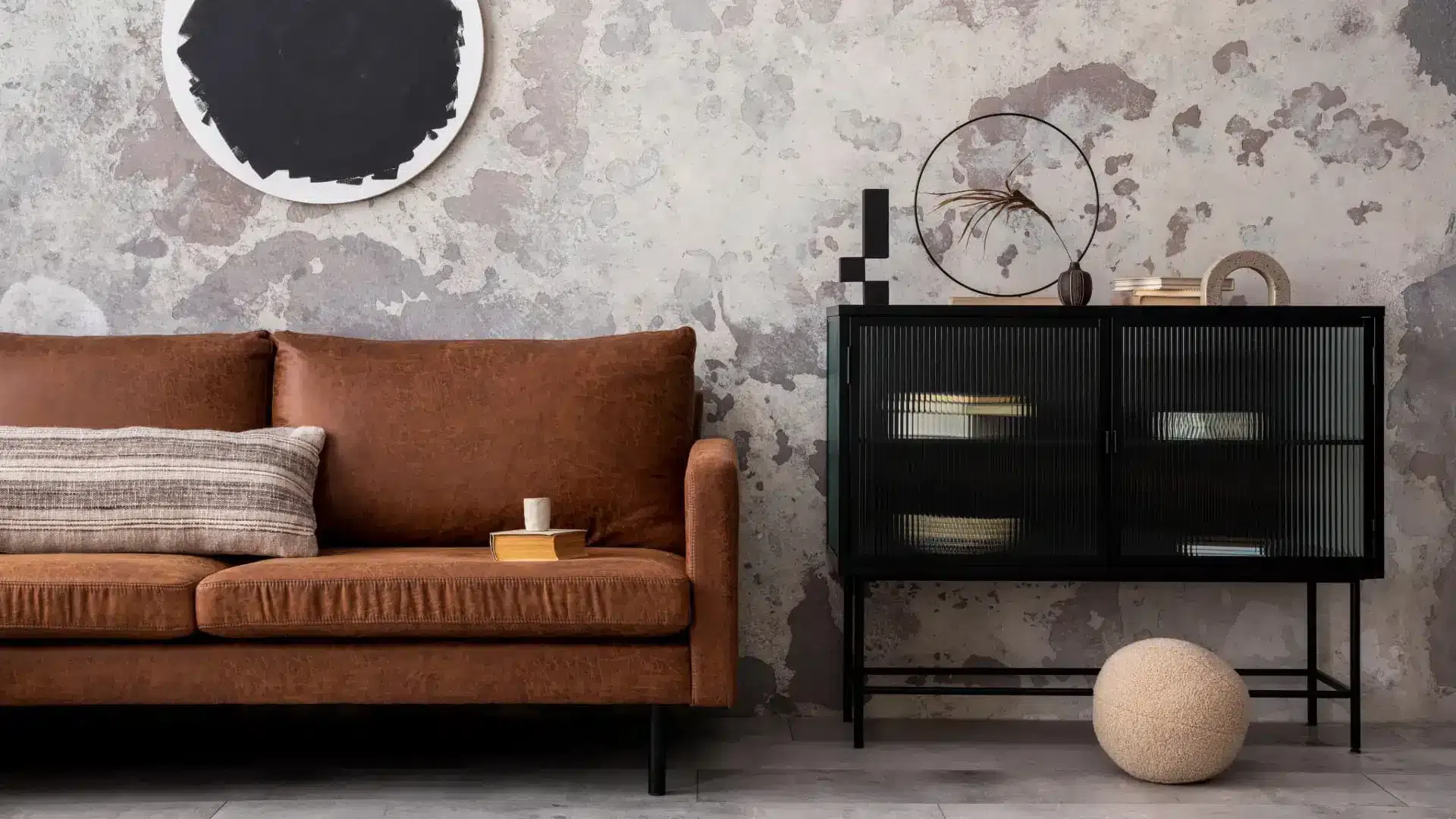 Design intérieur de loft industriel appartement avec canapé marron, commode noir, oreillers, décoration et accessoires personnels.