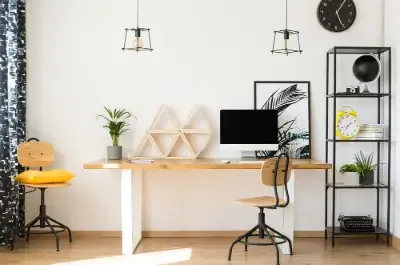 Oreiller jaune sur chaise en bois à côté d'une table au décor géométrique et bureau dans une zone de travail neutre.