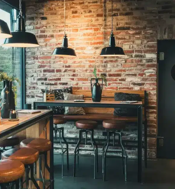 Coin salon avec tables de bar et chaises de bar dans un café moderne, style industriel avec mur en pierre, bois et acier noir.