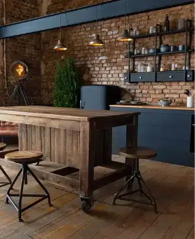 Vue latérale sur une table en bois et spacieuse cuisine industrielle loft au décor vintage et armoires noires.