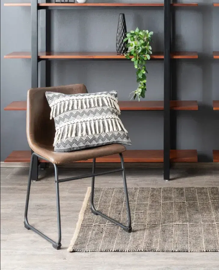 Salon élégant avec chaise de salle à manger en cuir, bibliothèque en bois, échelle murale bibliothèque avec décoration à la maison, parquet et tapis marron, contre un mur gris.