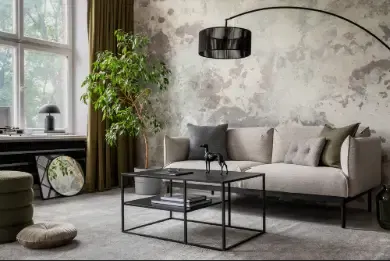 Intérieur de salon industriel et loft avec mur en béton, canapé gris, fauteuil moderne, table basse noire simple, oreillers verts, rideau, livres et accessoires personnels.