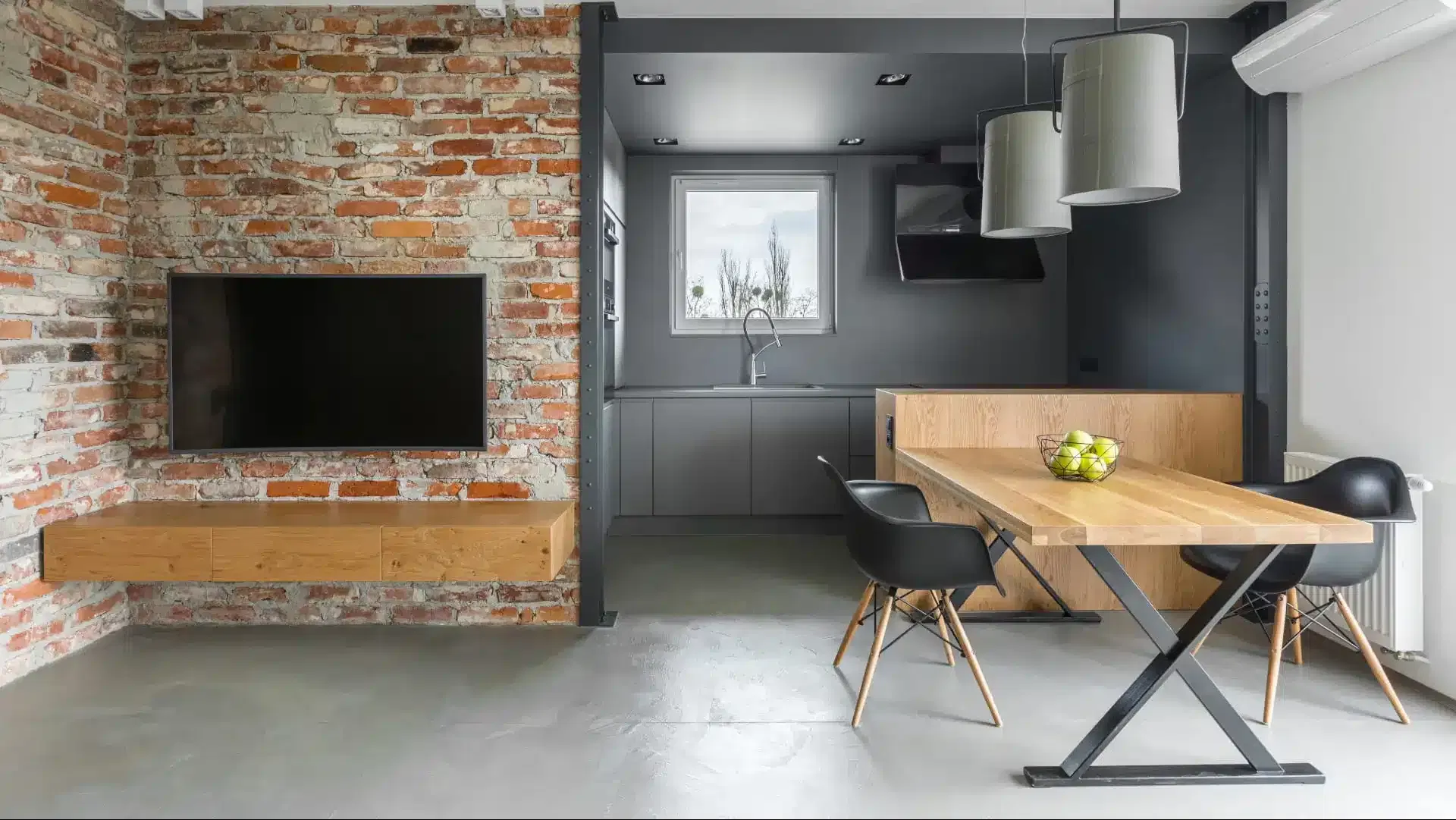 Intérieur de style industriel avec kitchenette, télévision, table, chaises et mur en brique.