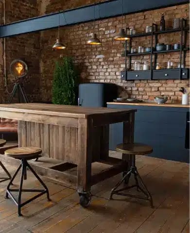 Vue latérale sur une table en bois et spacieuse cuisine industrielle loft au décor vintage et armoires noires.